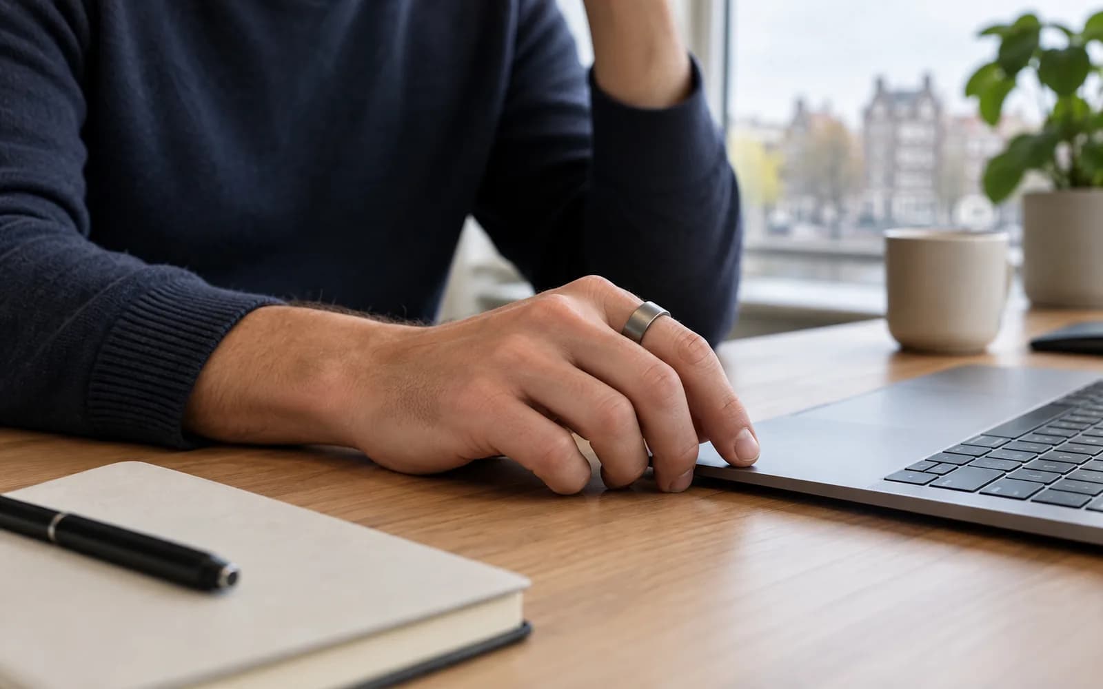 Illustration: Smart ring worn on a hand resting beside a laptop.