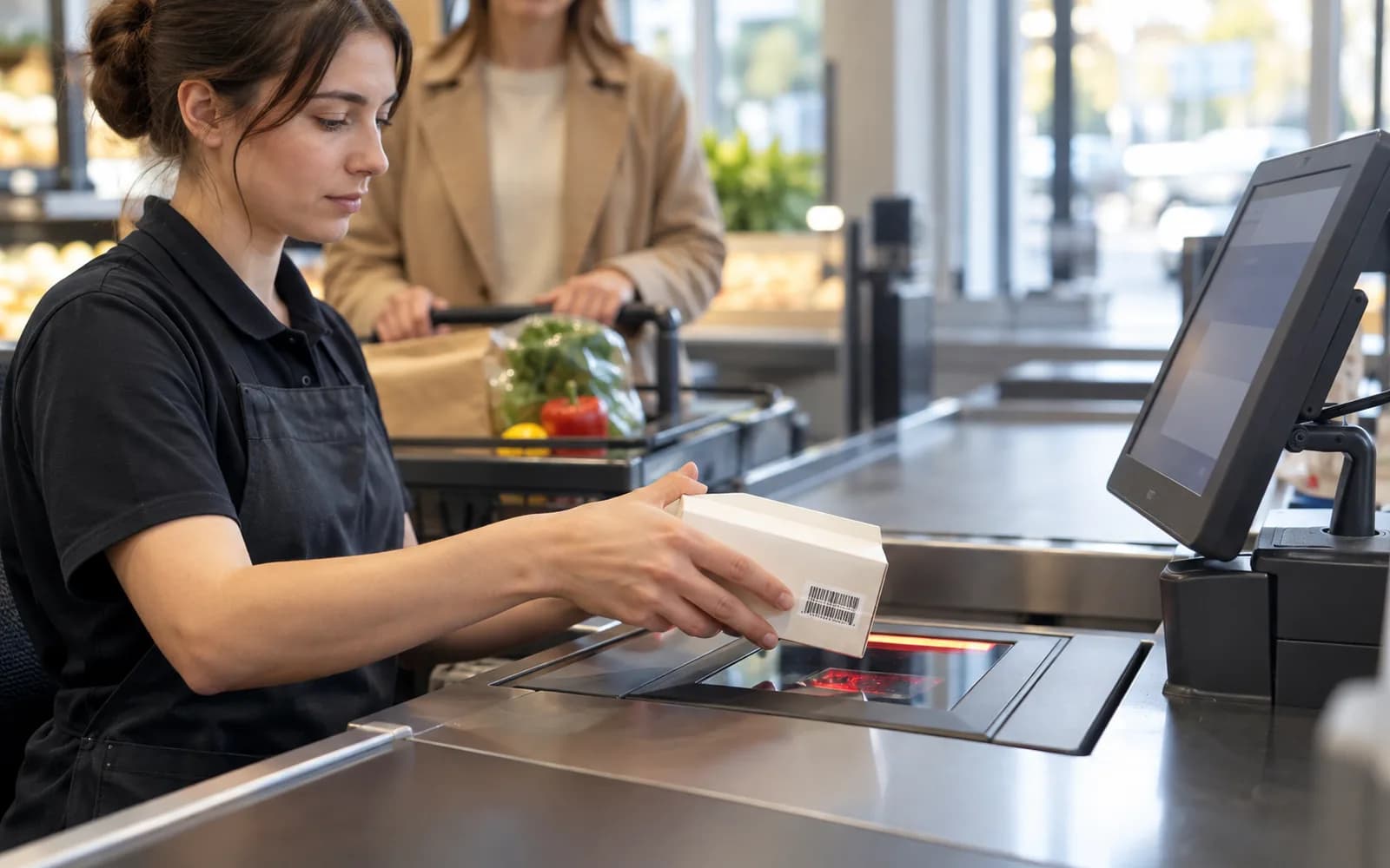 Illustration: Cashier passing a carton over a fixed checkout scanner.