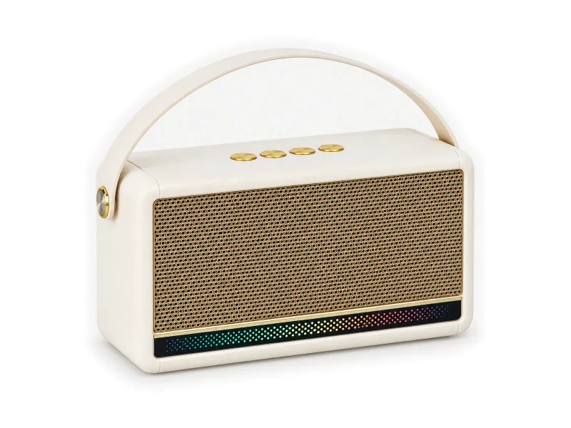 Ivory portable retro speaker with gold grille, arched strap and dotted light bar on a light studio background